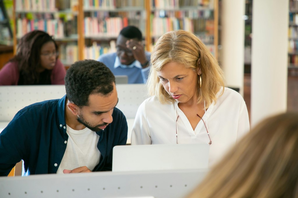 Person Helping another person with their Computer in an office or library setting.